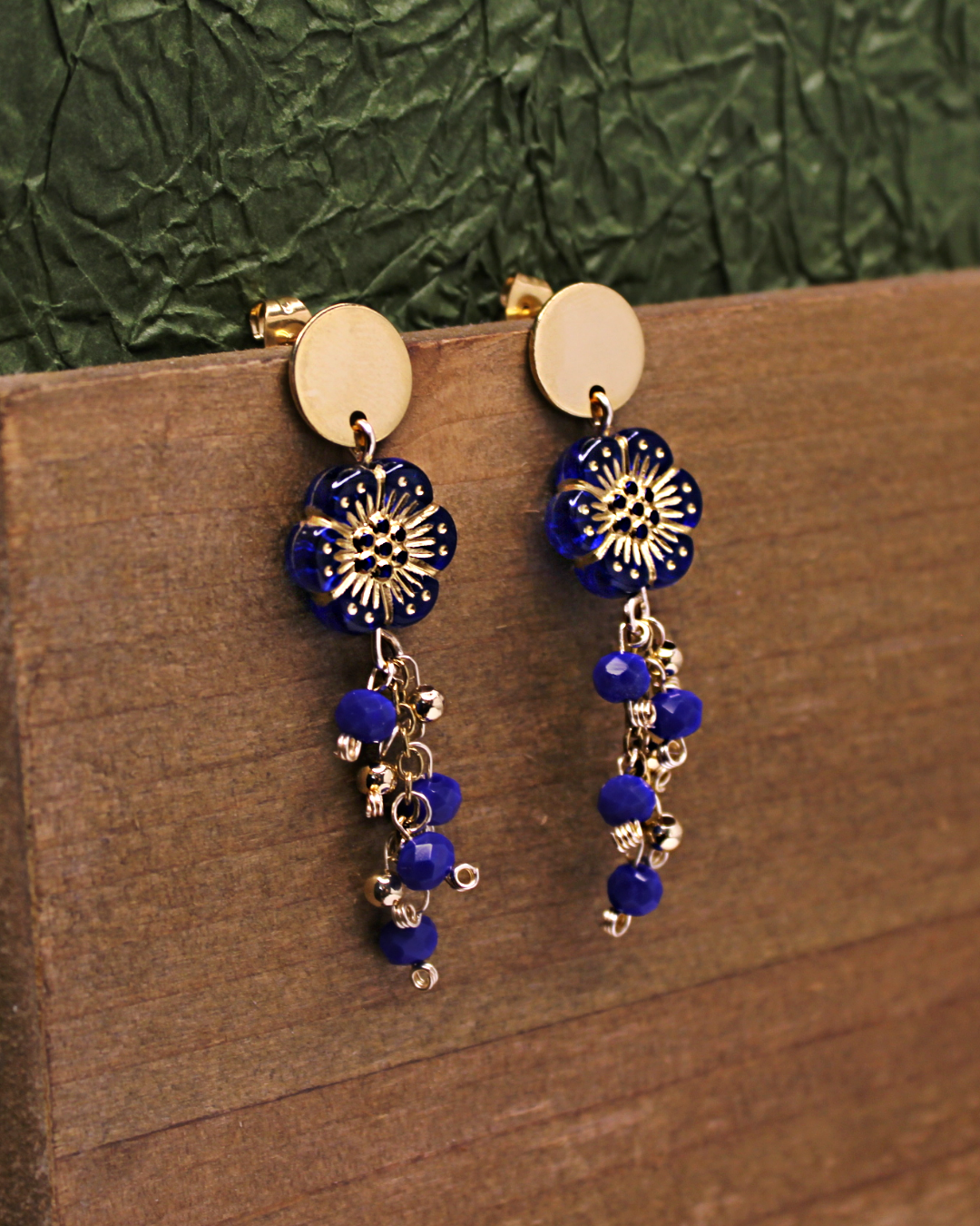 Gold plated stainless steel circle stud earrings with transparent dark blue flower beads with gold outline detail. Dangling earrings with chain and dark blue faceted bead accent.