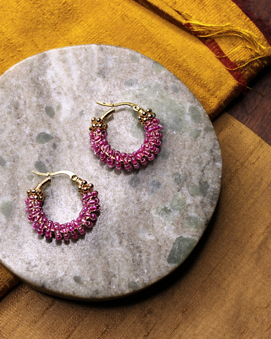 Small stainless steel gold colored hoop earrings with transparent pink crystal seed beads.