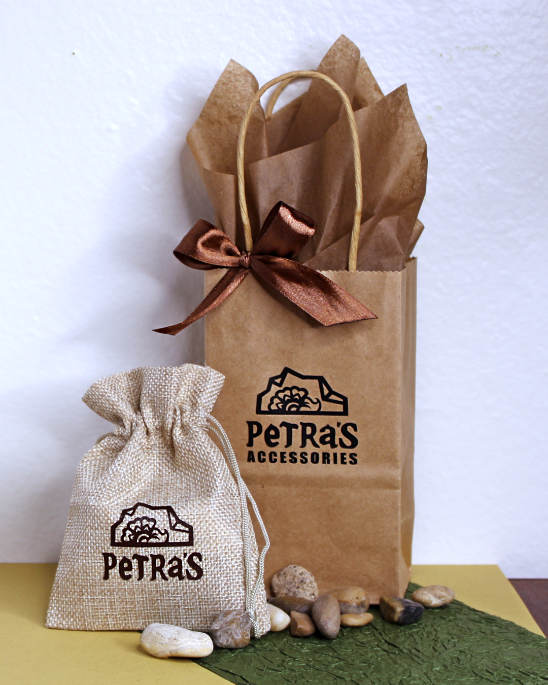 Jewelry giftwrap. Drawstring beige pouch with PeTRa'S ACCESSORIES logo. Brown kraft bag with PeTRa'S ACCESSORIES logo. Brown satin bow and brown tissue paper.
