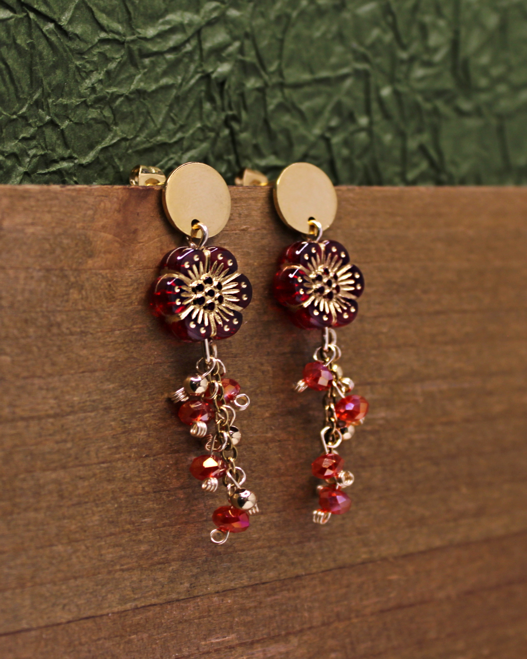 Gold plated stainless steel circle stud earrings with transparent red flower beads with gold outline detail. Dangling earrings with chain and red faceted bead accent.