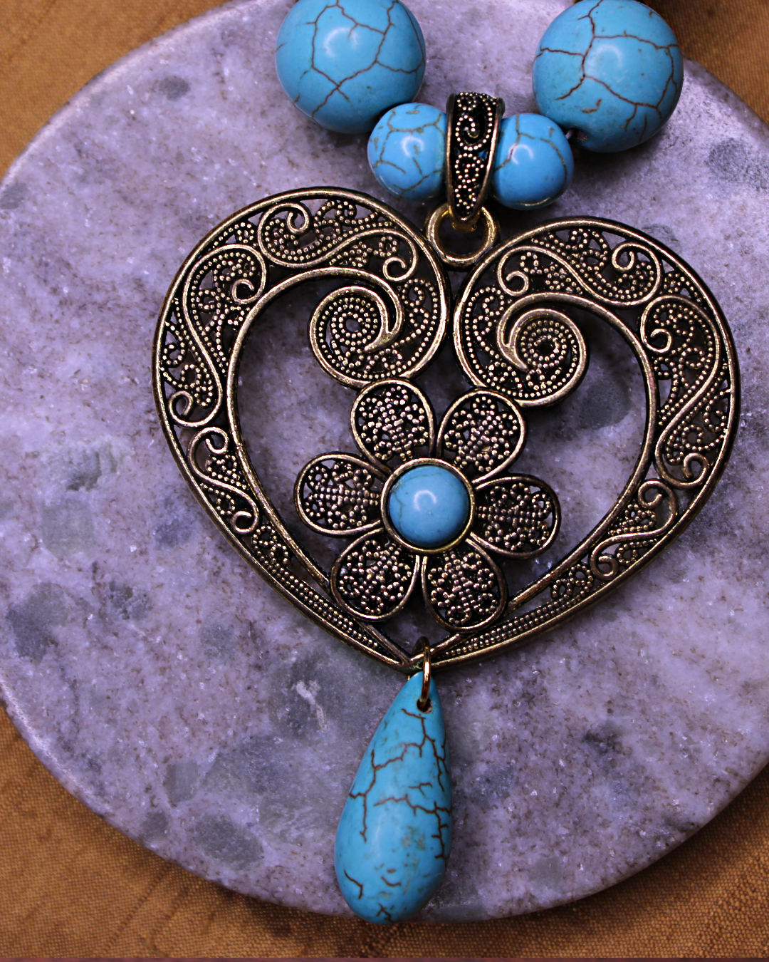 Detail picture of statement turquoise color necklace with filigree antique gold heart pendant and a teardrop turquoise dangling bead. 
