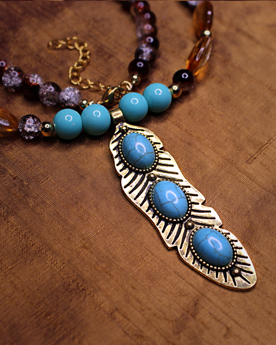 Detail picture of  antique gold color large feather pendant necklace with three turquoise center details and  brown, amber, gold, turquoise and  marigold beads.