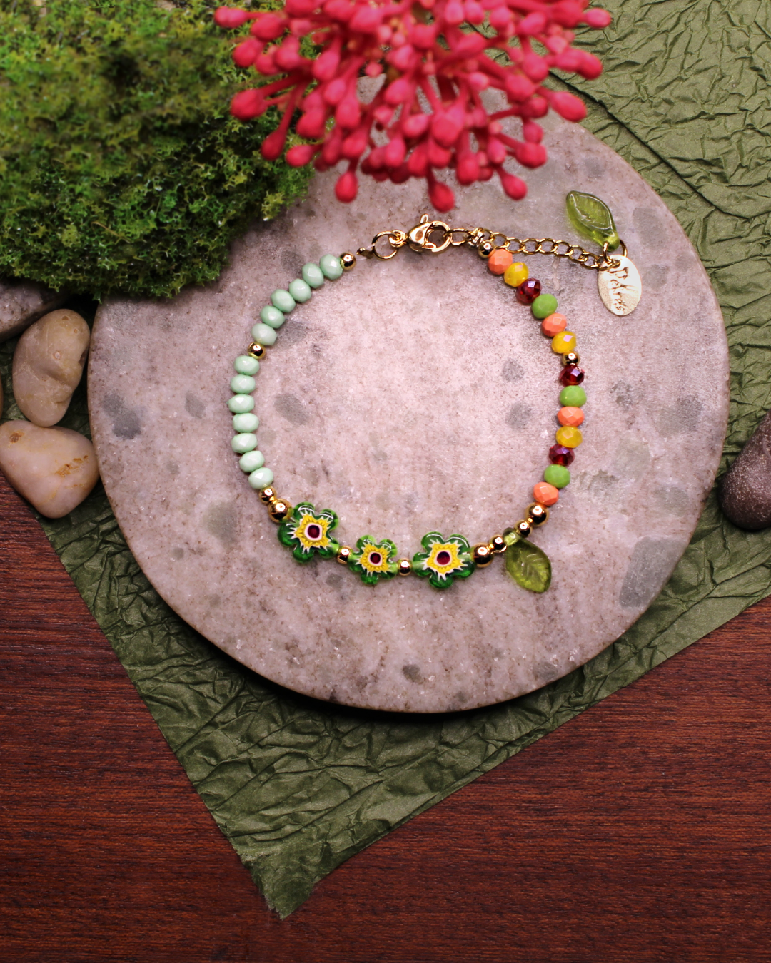 Colorful bracelet made of faceted crystal beads in colors: yellow, red,  apple green, tangerine, mint green  and millefiori beads. Bracelet on top of a gray stone display. Natural red flower, rocks, green and brown background.