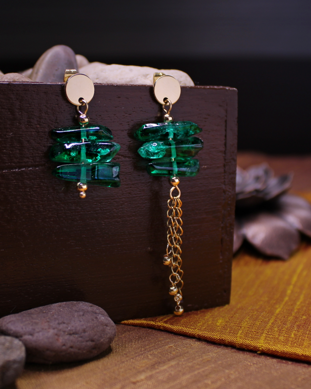 Gold plated stainless steel round stud asymmetrical earrings with green crystals and dangling gold chain accent. 