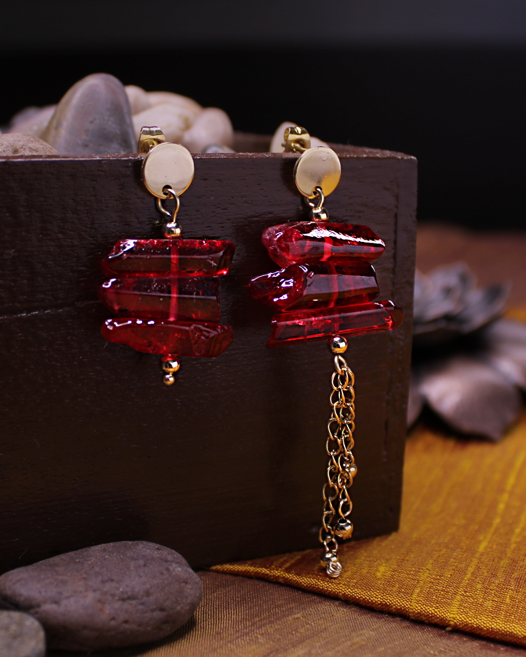 Gold plated stainless steel round stud asymmetrical earrings with red crystals and dangling gold chain accent. 