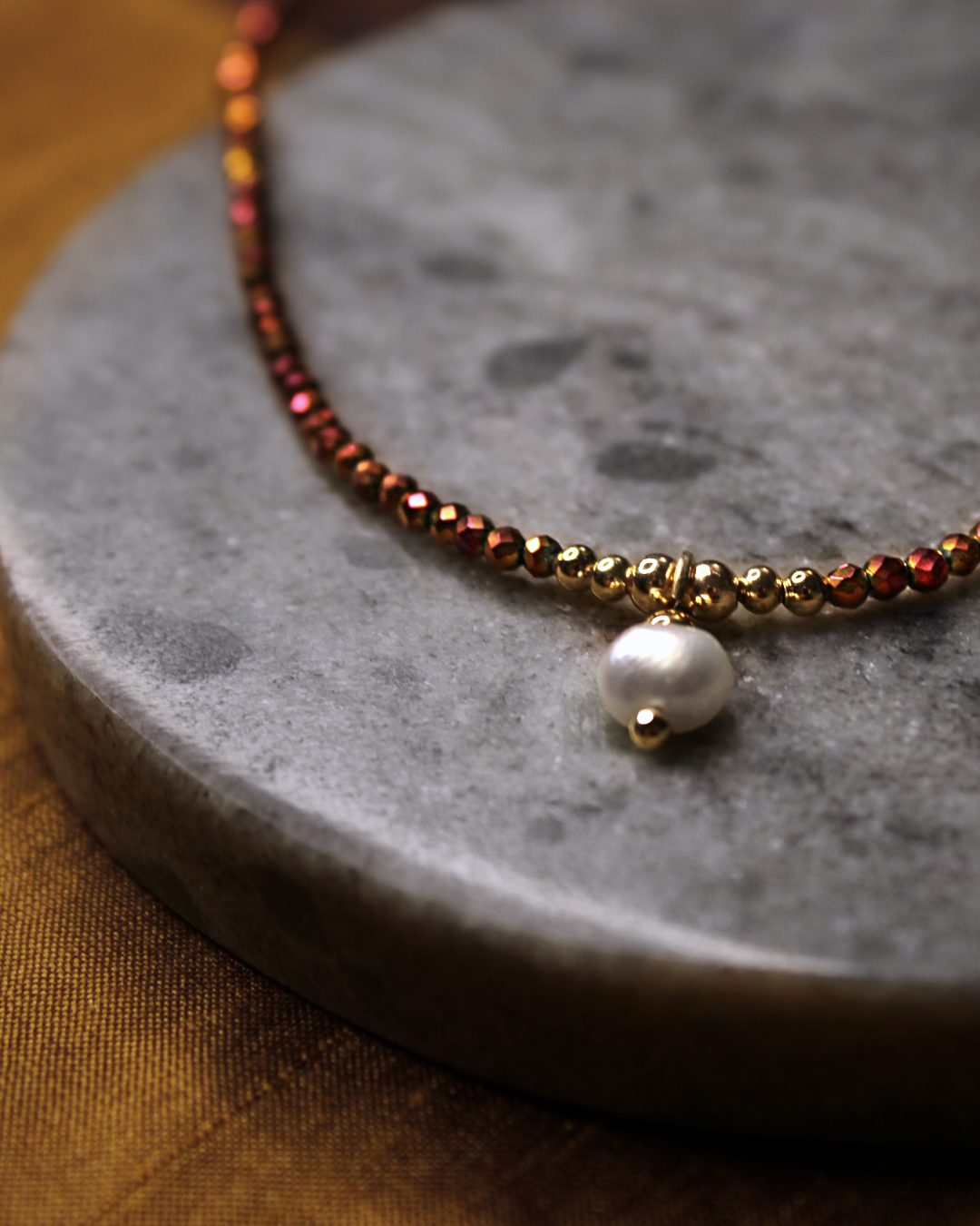 Detail of dainty necklace with small faceted copper color crystal beads and dangling freshwater pearl charm.